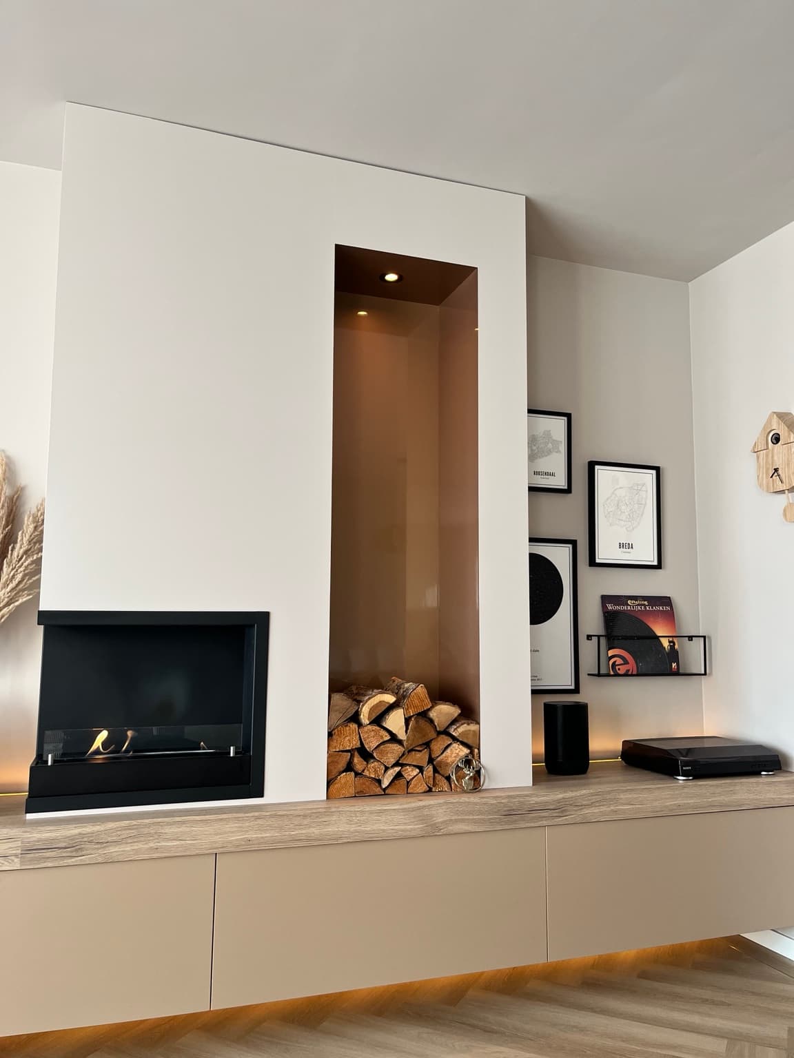 Warm finished media wall combining wood, taupe cabinetry, a black fireplace, logs and soft lighting.